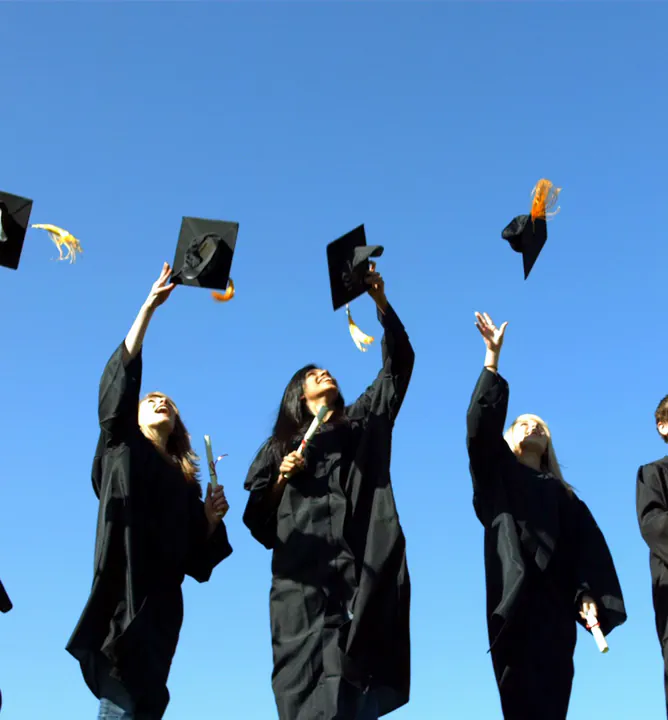 Graduates in gowns throw their caps into a blue sky.
