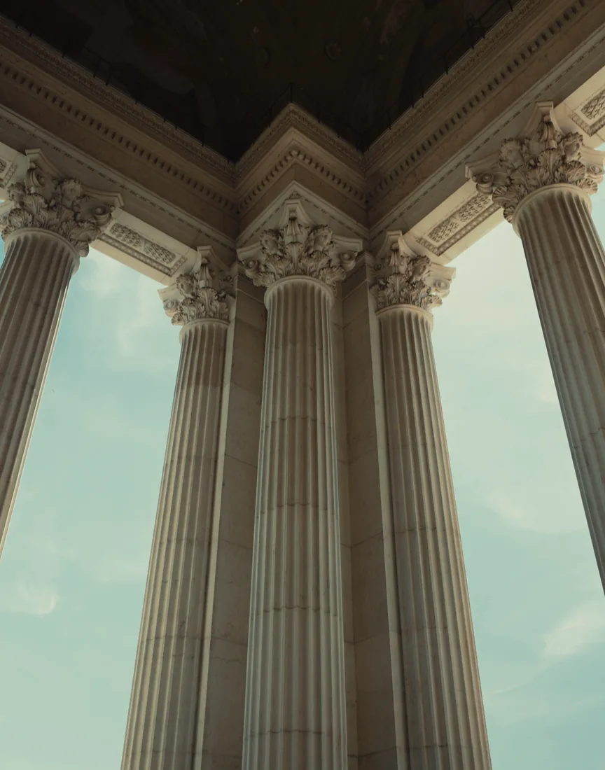 Classical stone columns rising into a pale sky, from below.