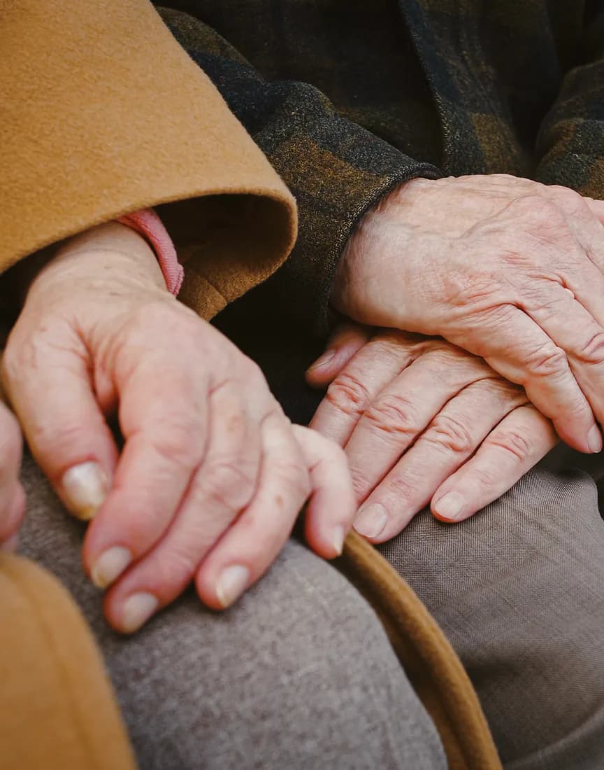 An older couple’s hands resting together on their knees.