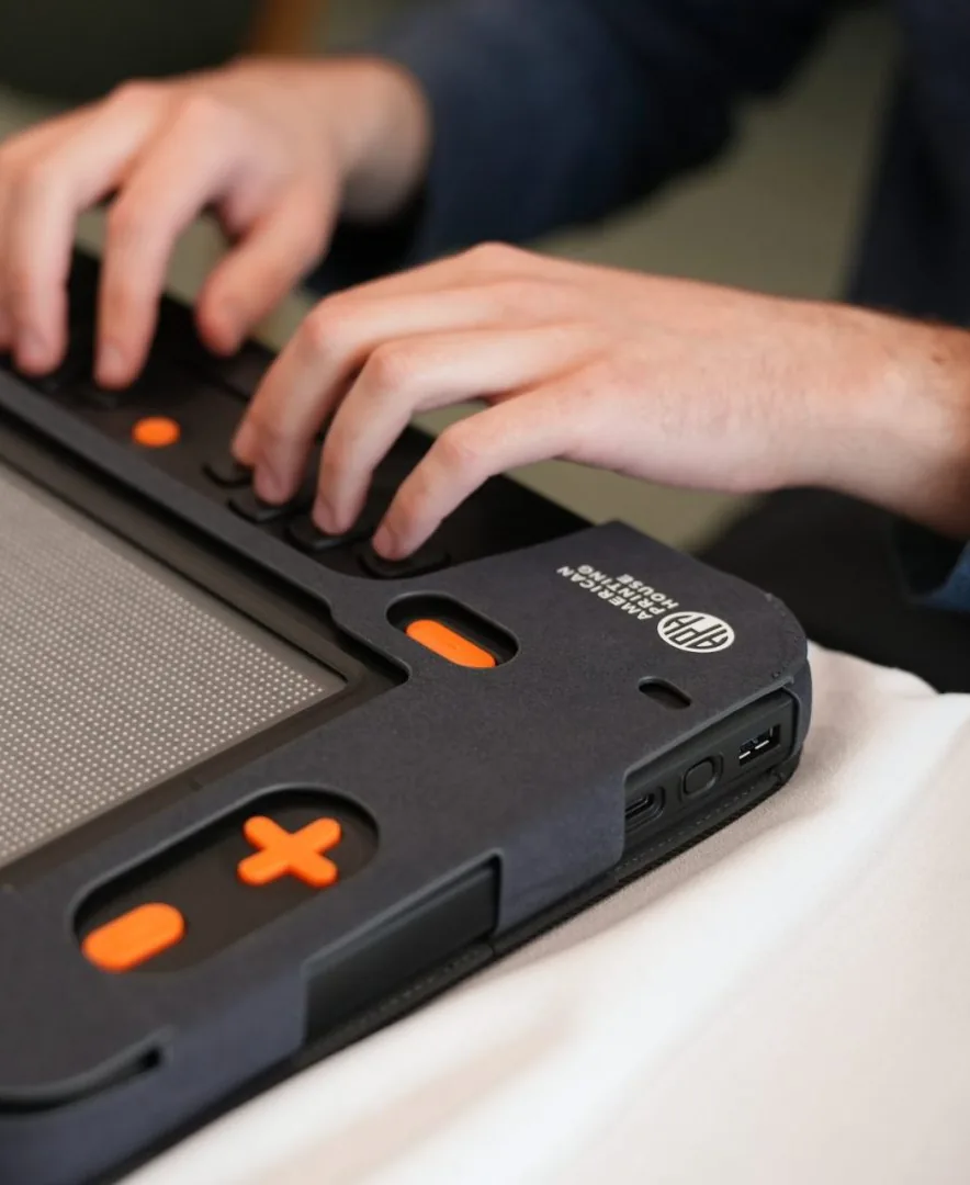 Hands reading on a braille display with orange navigation keys.