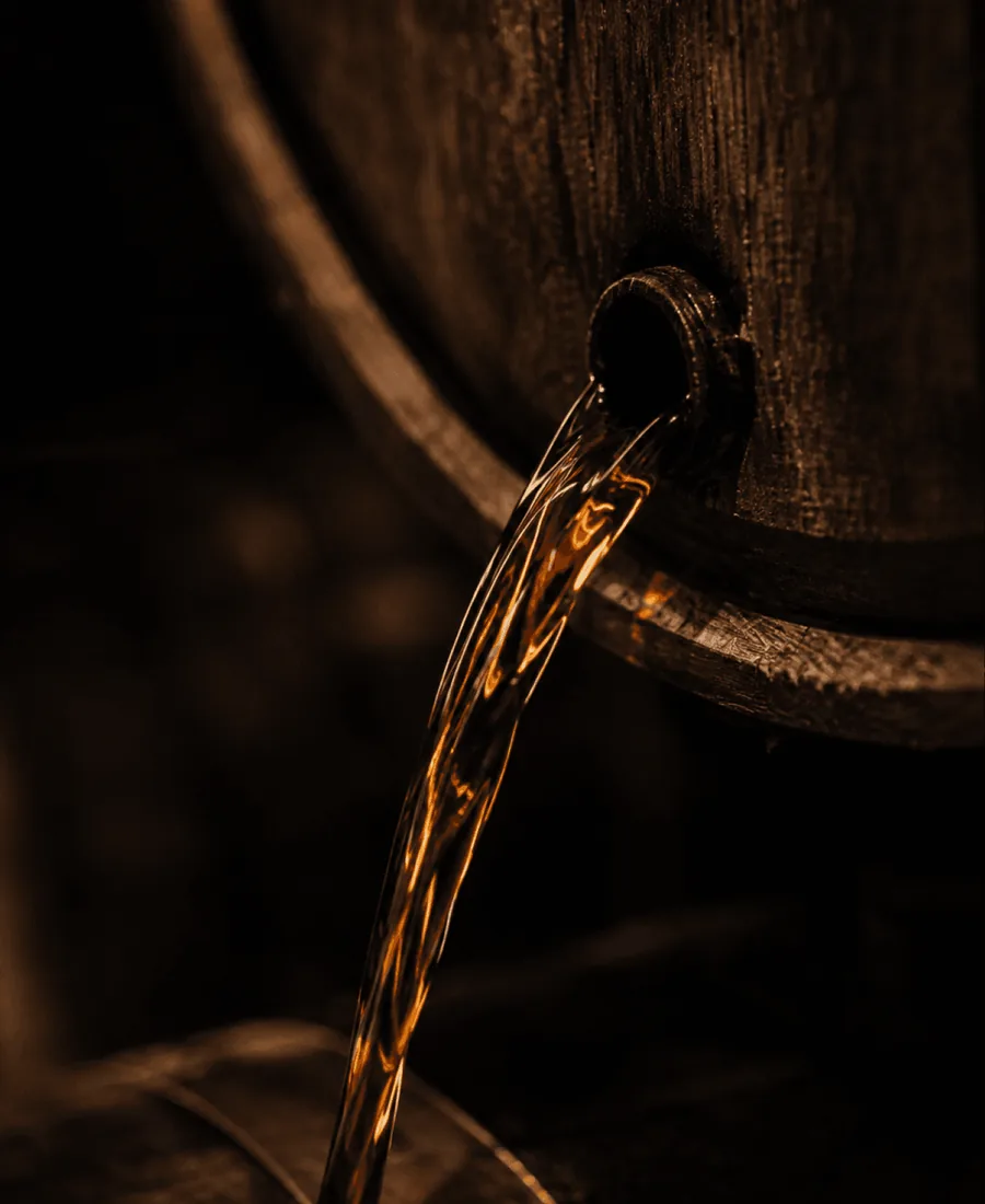 Spirit pouring from the tap of an oak barrel in low, warm light.