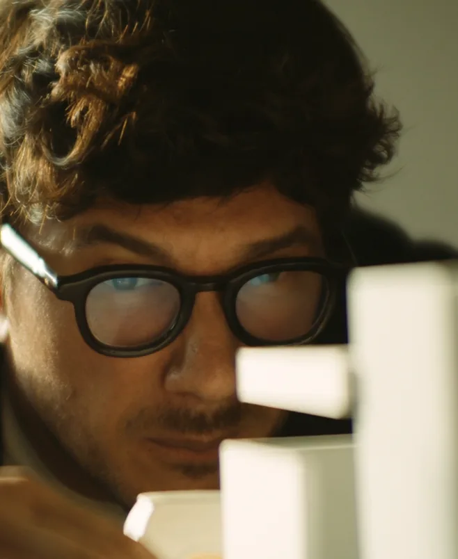 A man in dark-rimmed glasses studies a model built from white blocks, close up.
