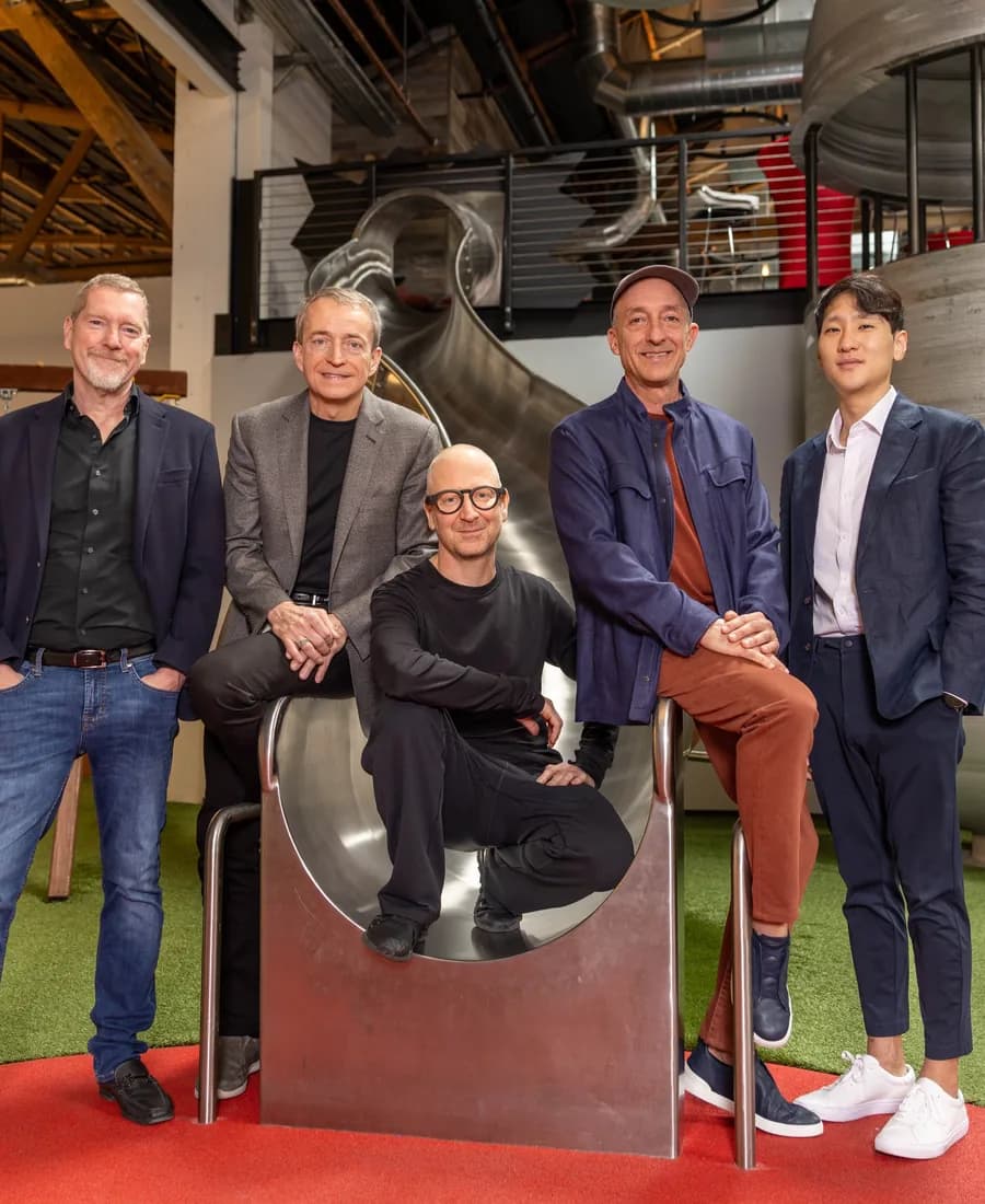 Five people pose around a sculpture in a bright, industrial workspace.