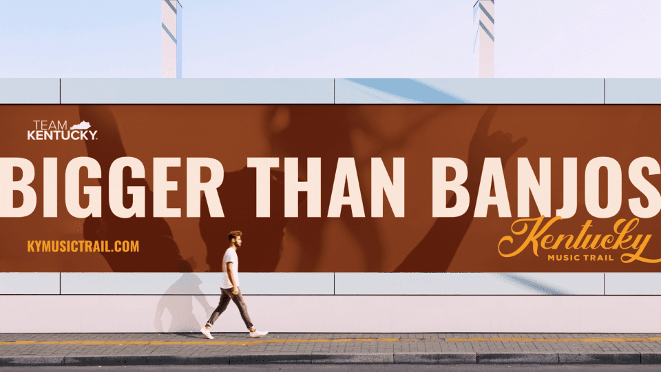 Street-level billboard displaying Bigger Than Banjos campaign with pedestrian