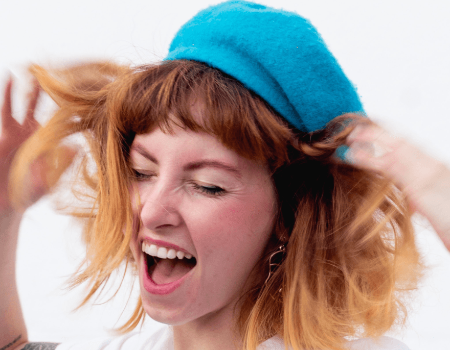 Joyful young woman with red hair wearing a teal beret, expressing excitement and personality