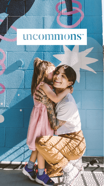 Mobile lifestyle image of two friends embracing against colorful mural with logo overlay