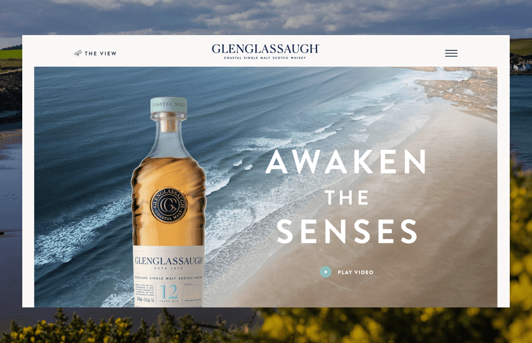 Desktop homepage hero featuring the Awaken the Senses headline with a coastal beach panorama and whisky bottle