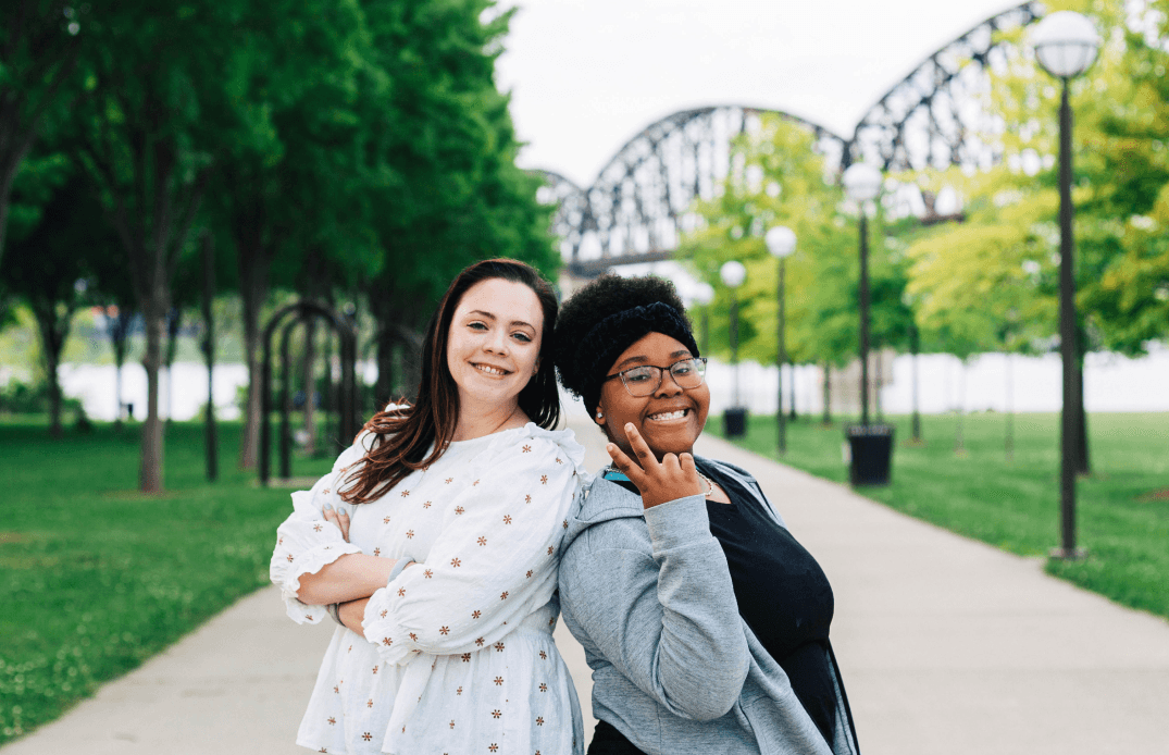 Two women smiling and embracing in a park with Louisville bridge visible in background