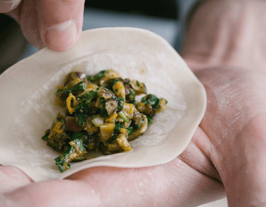 Close-up detail shot of hands cradling a fresh dumpling wrapper filled with savory vegetable and meat mixture