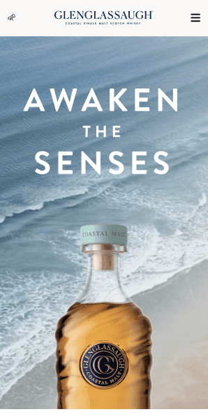 Mobile homepage hero with Awaken the Senses headline and whisky bottle on sandy beach