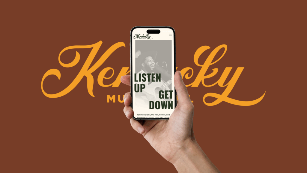 A hand holding a mobile phone displaying the Kentucky Music Trail homepage.
