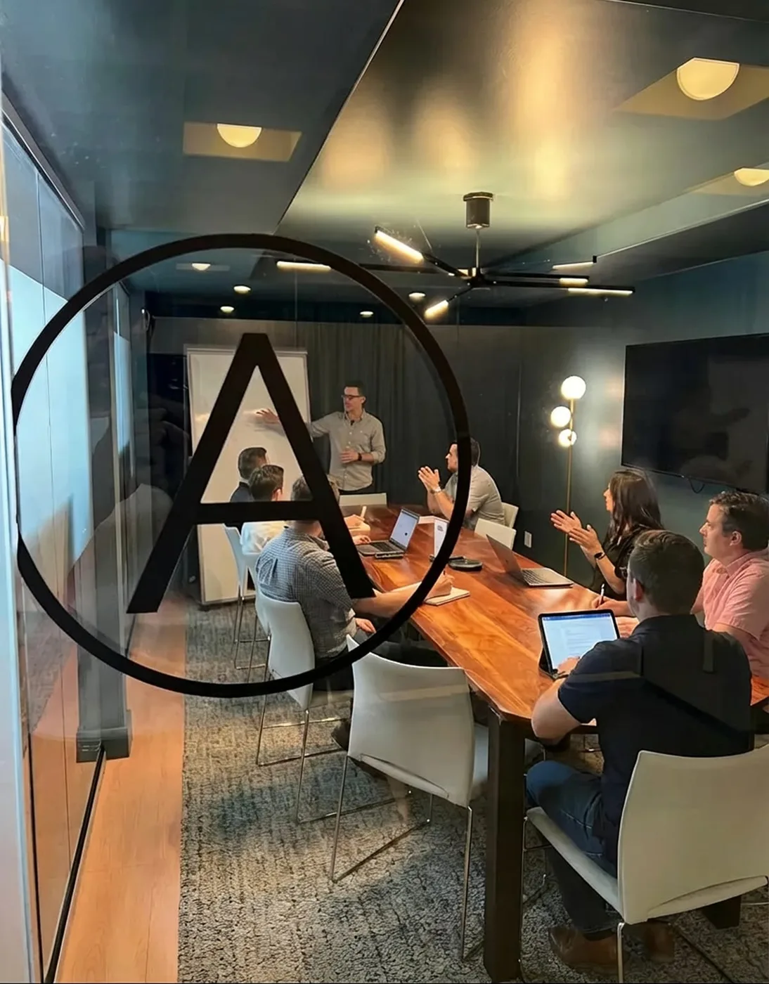 A team meeting around a long wooden table in the conference room, seen through its glass wall