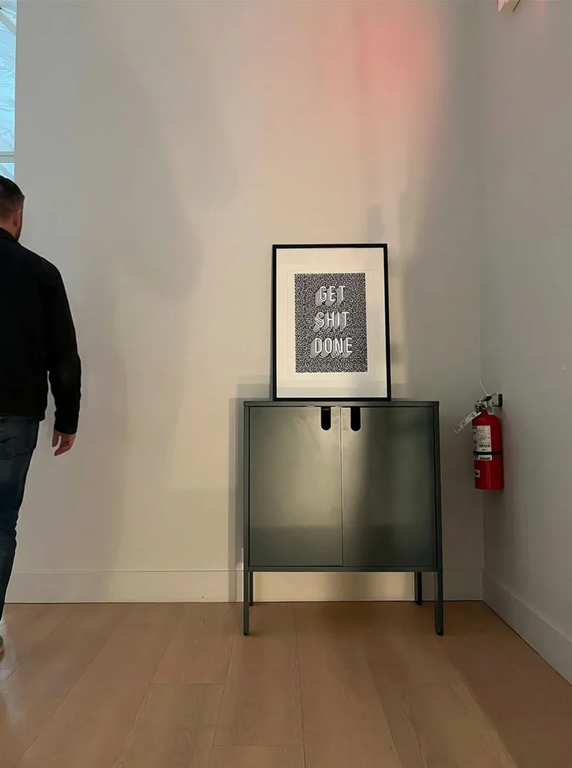 A framed “Get Shit Done” print on a green cabinet against a white wall