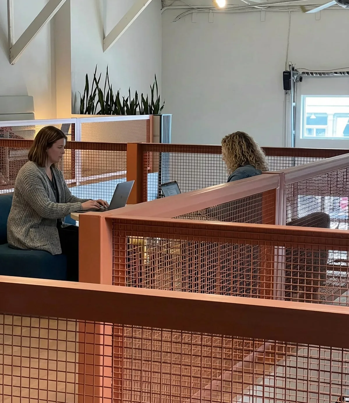 Two people working at laptops behind the mezzanine's copper mesh railing
