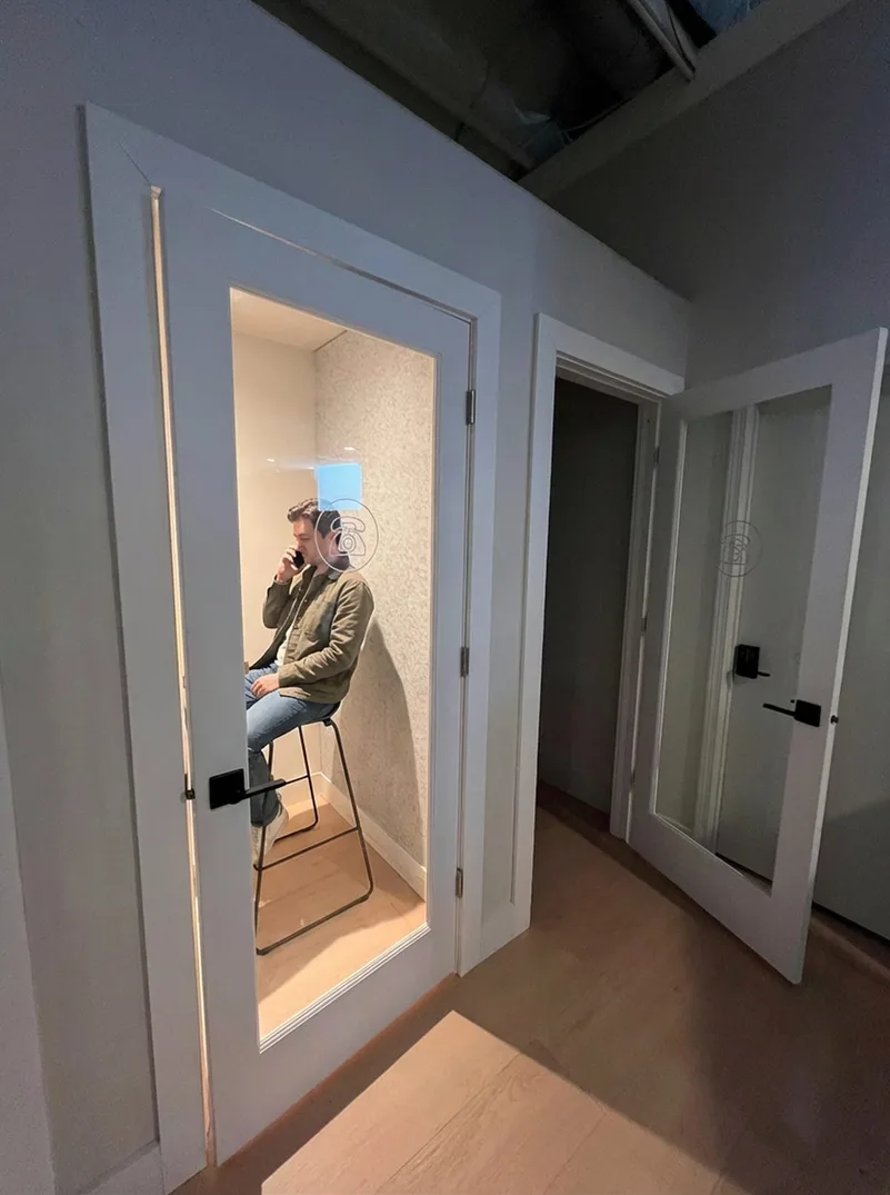 Someone on a call in a phone booth, sitting on a stool
