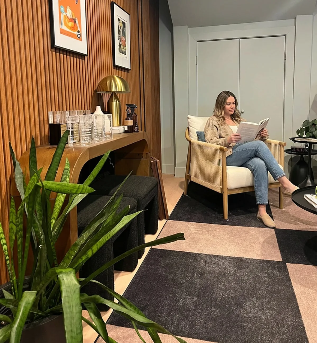 Someone reading in an armchair in a quiet corner with slatted wood walls, framed posters and a plant