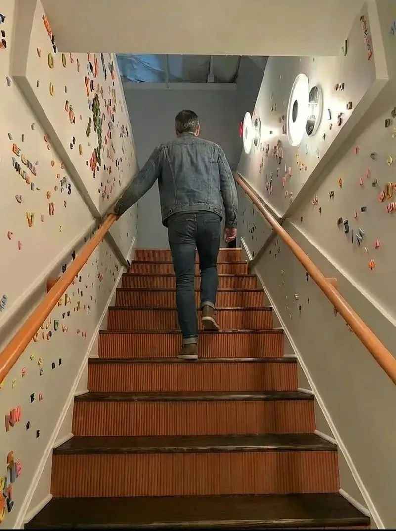 Someone climbing the stairs to the mezzanine, the walls either side covered in magnetic letters