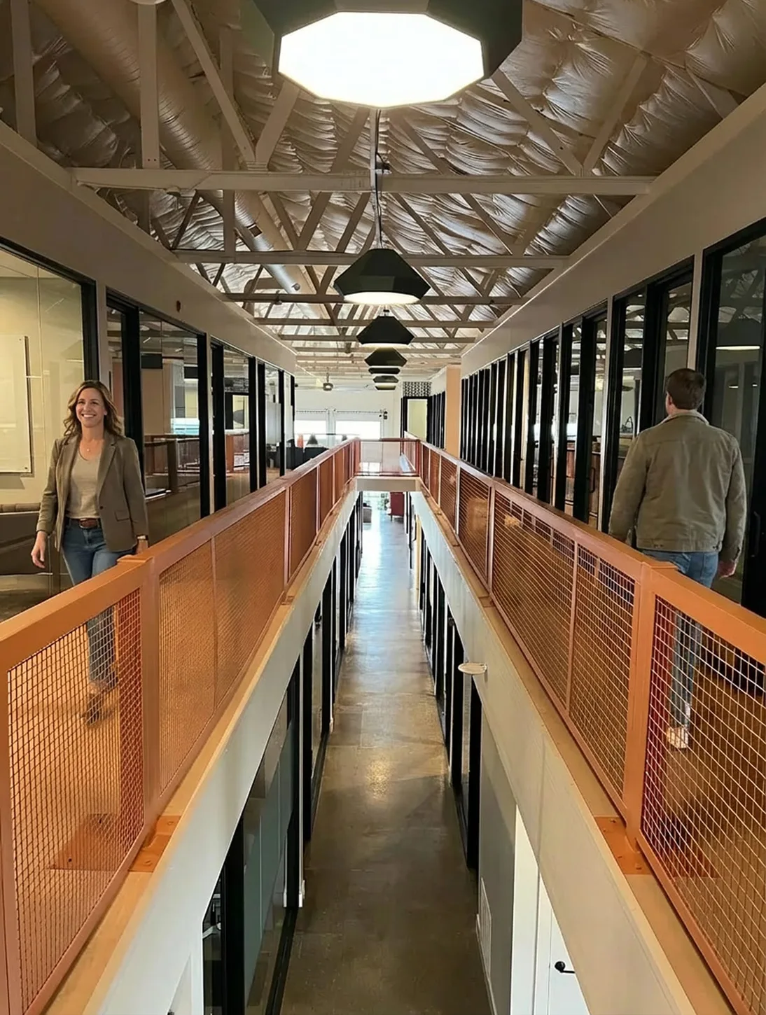 The mezzanine walkway: copper mesh railings and glass-walled offices, a teammate walking towards the camera