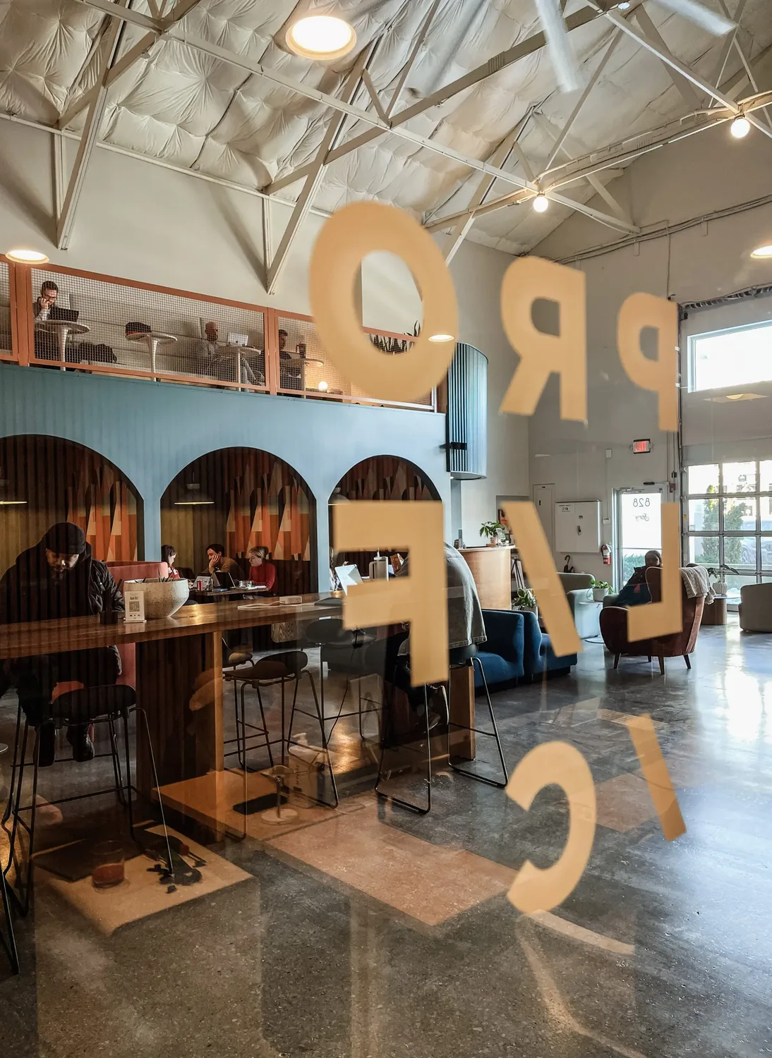 The studio seen through a glass wall lettered “Prolific”: people working at a high table in front of the arched booths